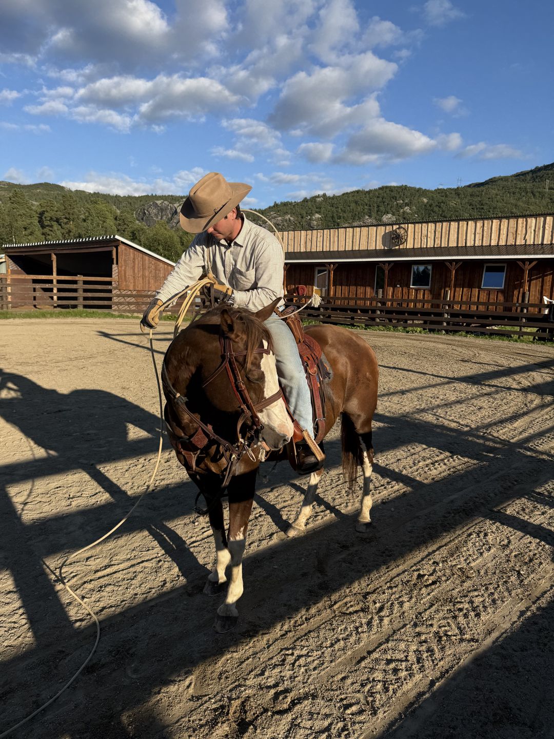 A cowboy with a lasso on horseback in the arena at Flatmoen